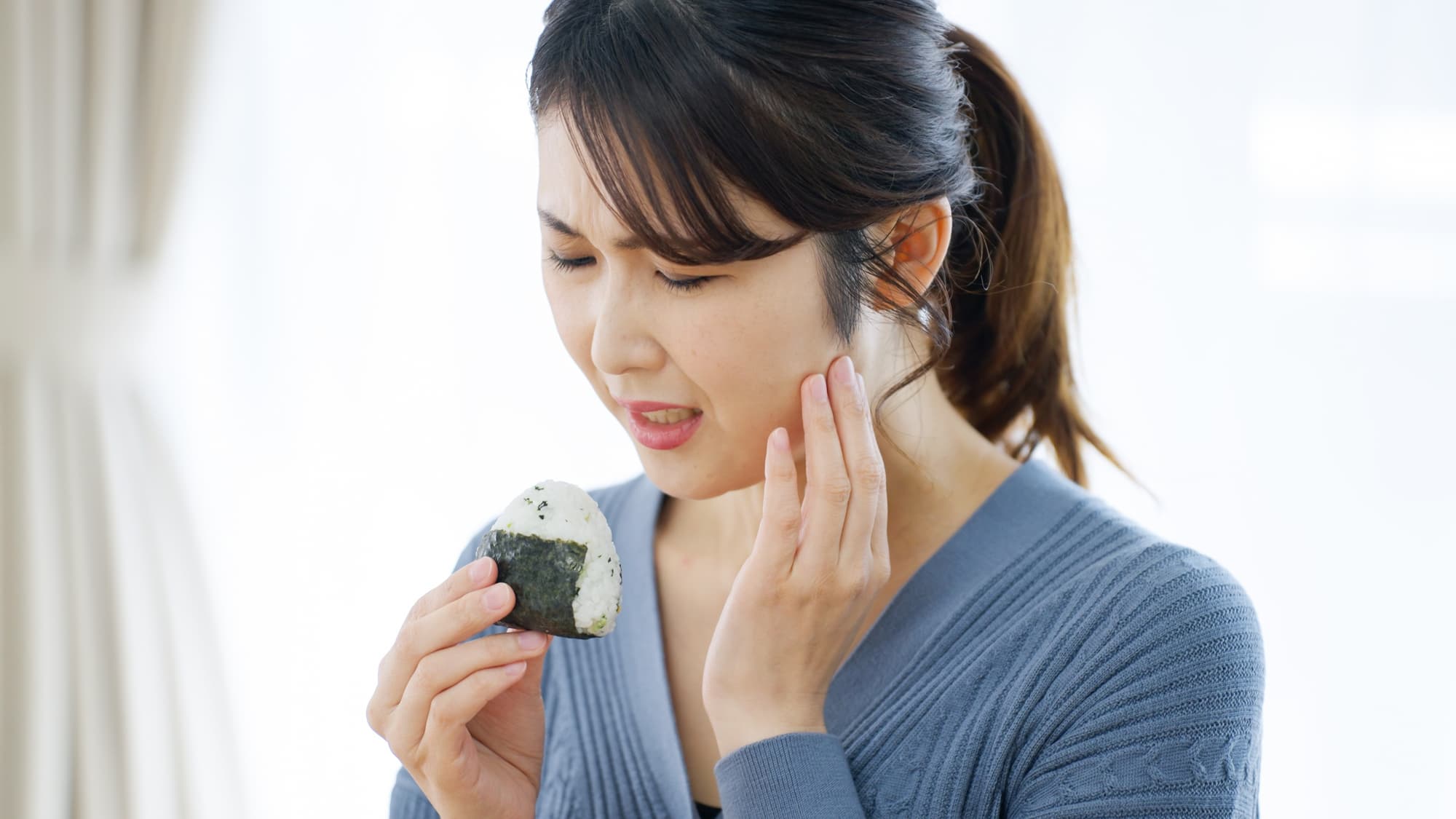 おにぎりを食べて顎が痛む女性